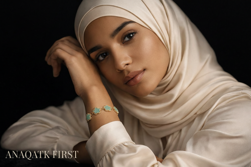 Woman wearing a beige hijab and white outfit with jewelry on a black background