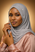 Woman wearing a light gray hijab with embellishments against a dark background