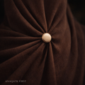Close-up of brown fabric with a button in the center, featuring the brand 'ANAQATK FIRST'.