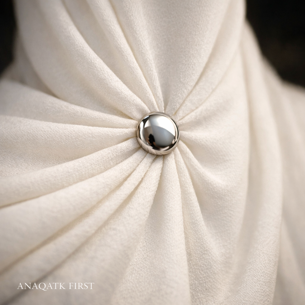 Close-up of a textured white fabric with a central button, featuring the brand 'ANAQATK FIRST'.