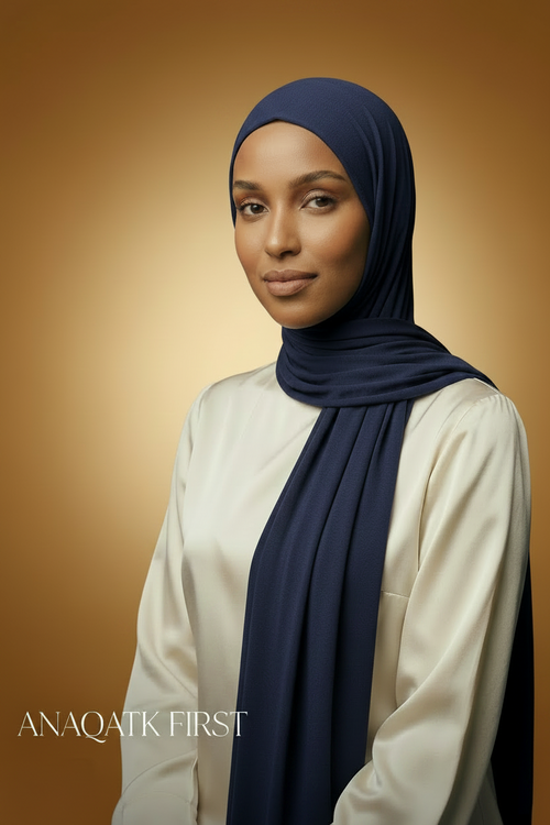 Woman wearing a brown hijab and beige top against a dark background with 'ANAQATK FIRST' text.