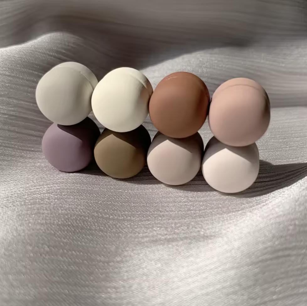 Set of nine round silicone beads in various pastel colors on a textured white surface.