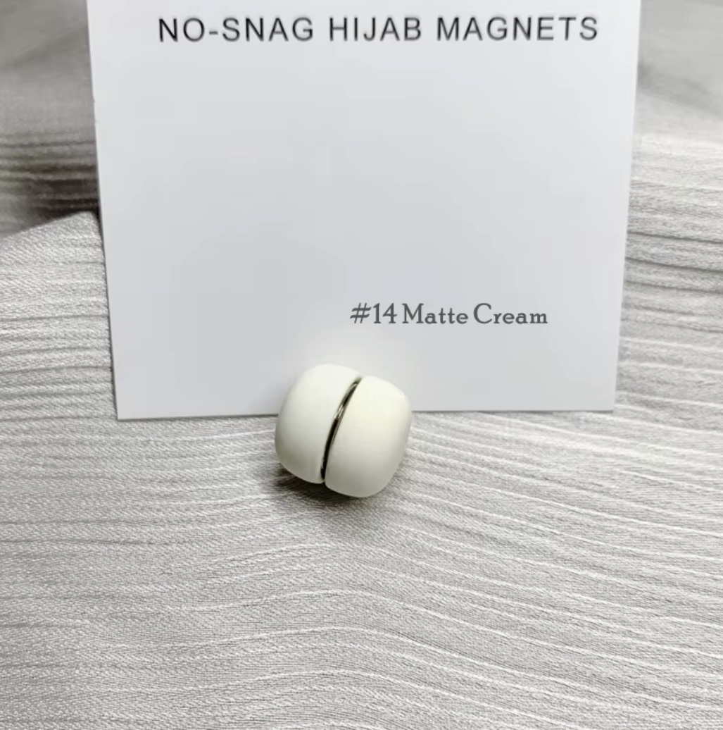 White hijab magnet with a card labeled 'No-Snag Hijab Magnets #14 Matte Cream' on a textured surface.