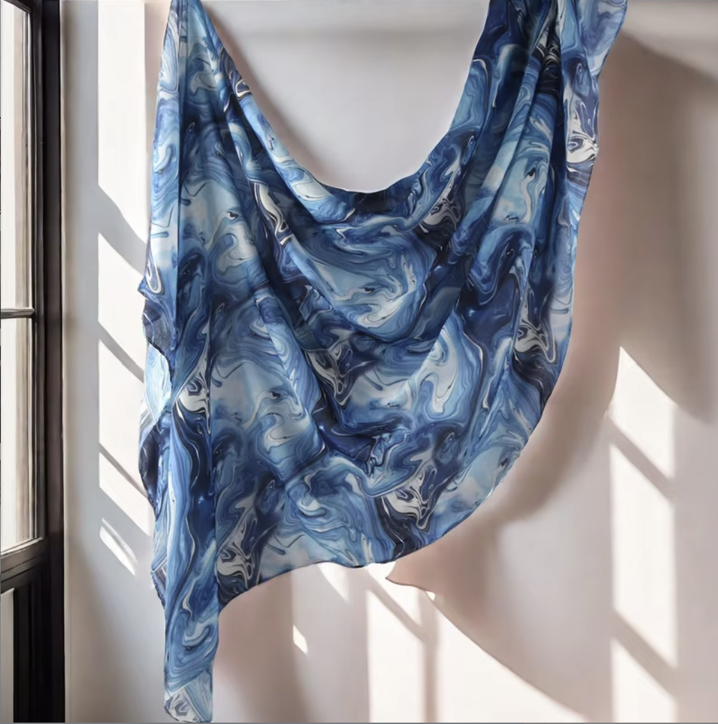 Blue marbled scarf draped over a mannequin against a window with sunlight filtering through.