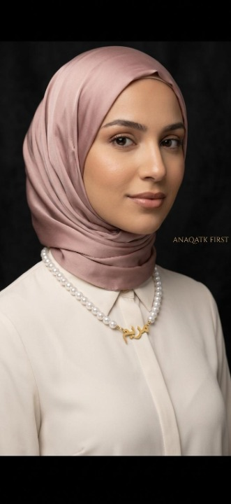 Woman wearing a pink hijab and pearl necklace against a black background